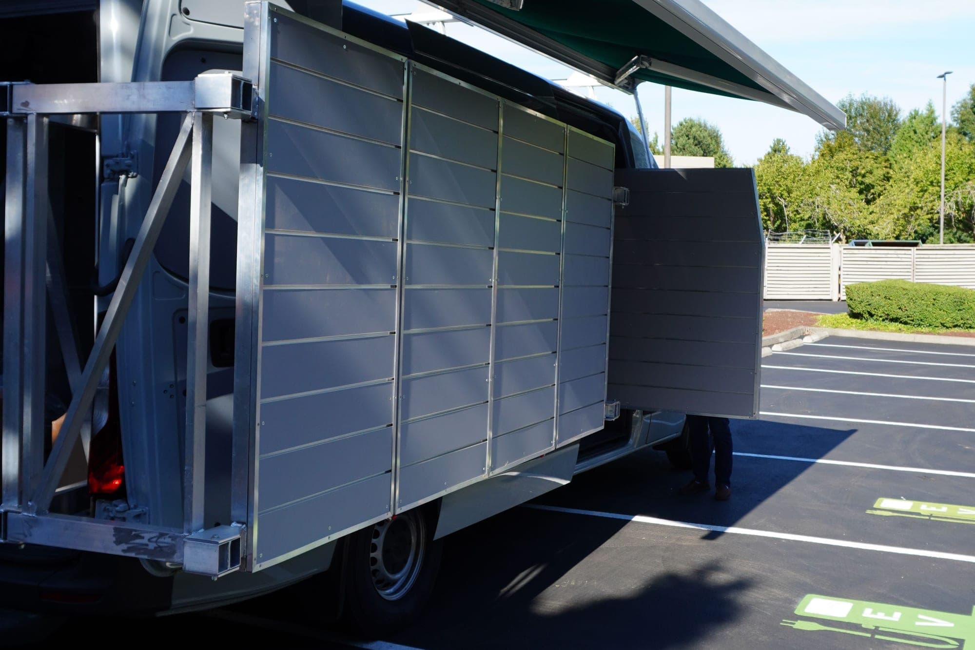 The van parked with its awning extended and the shelving panels folded out flat, still empty