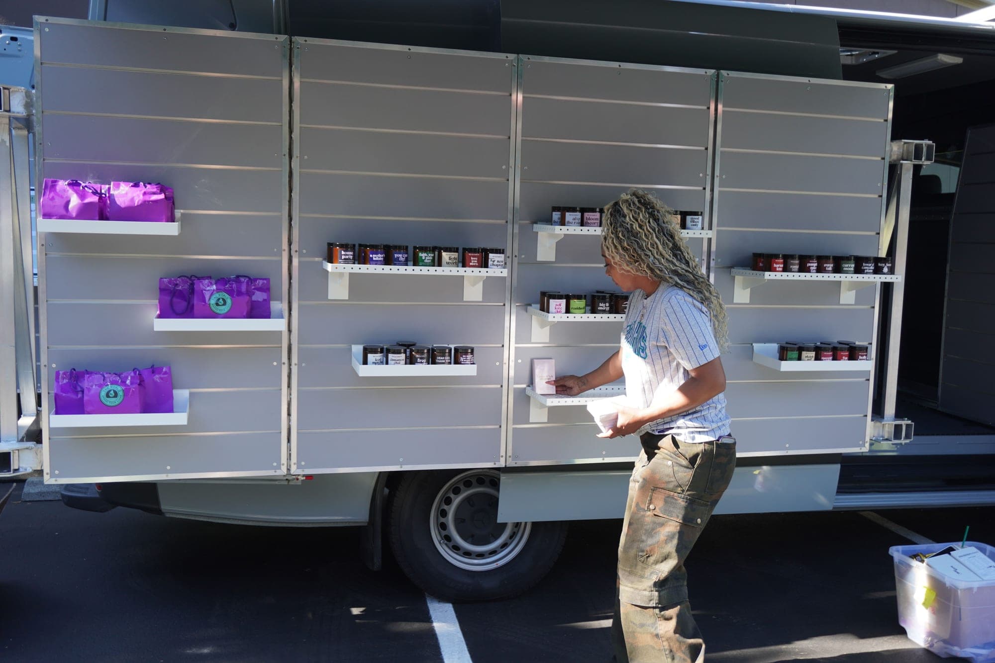 Colina setting out candles, skincare and purple gift bags along the van's shelves